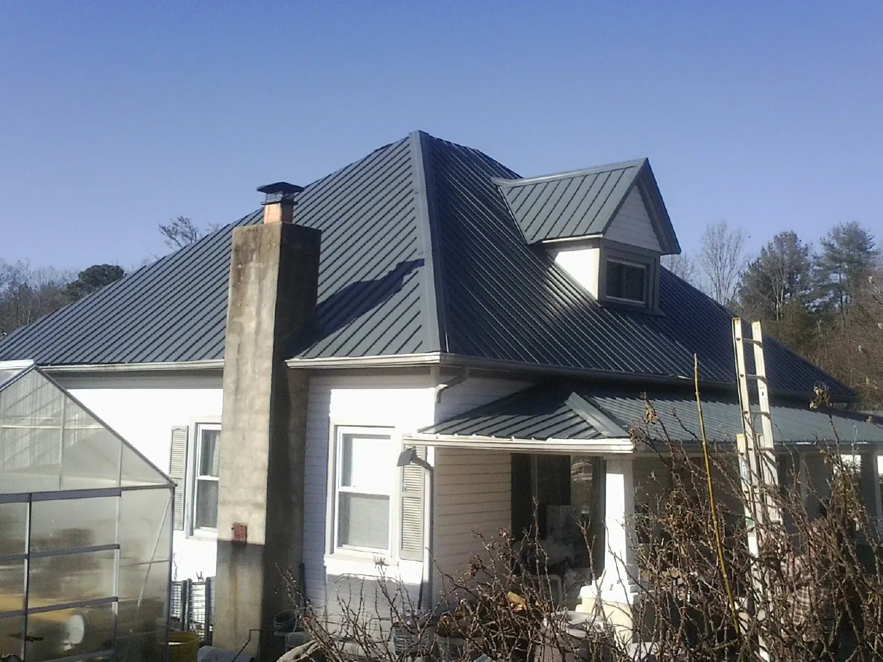 Dark blue standing seam metal roof on a white farmhouse with dormer — Slate & Tile Roof Repair by Roofing Brothers in Social Circle