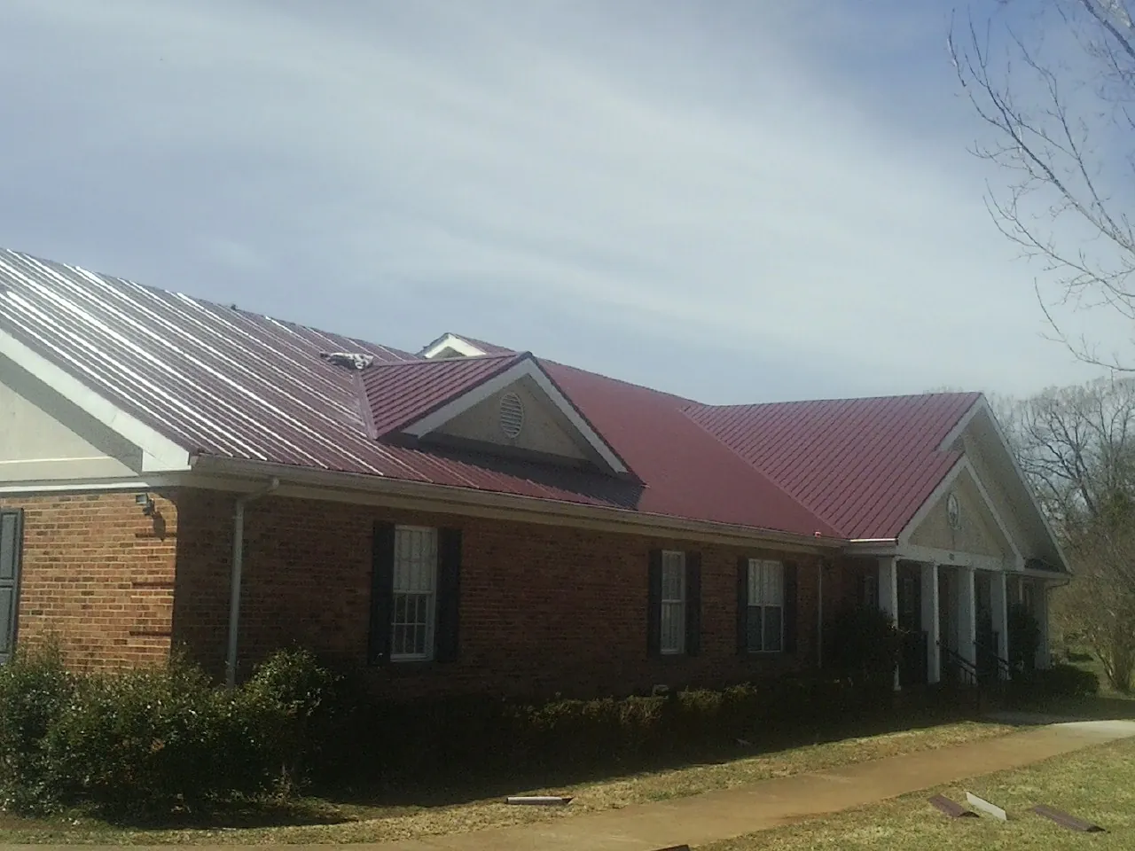 Red metal roof with gabled entries on a long brick building, from a Hail Damage Roof Repair job in Social Circle