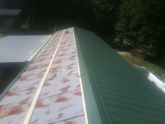 Old rusted panels beside newly installed green metal roofing — Wind Damage Roof Repair by Roofing Brothers in Social Circle