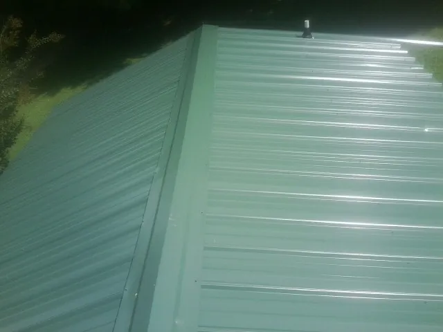 New green metal panels meeting at the ridge of a roof — Flat Roof Repair work by our crew in Social Circle