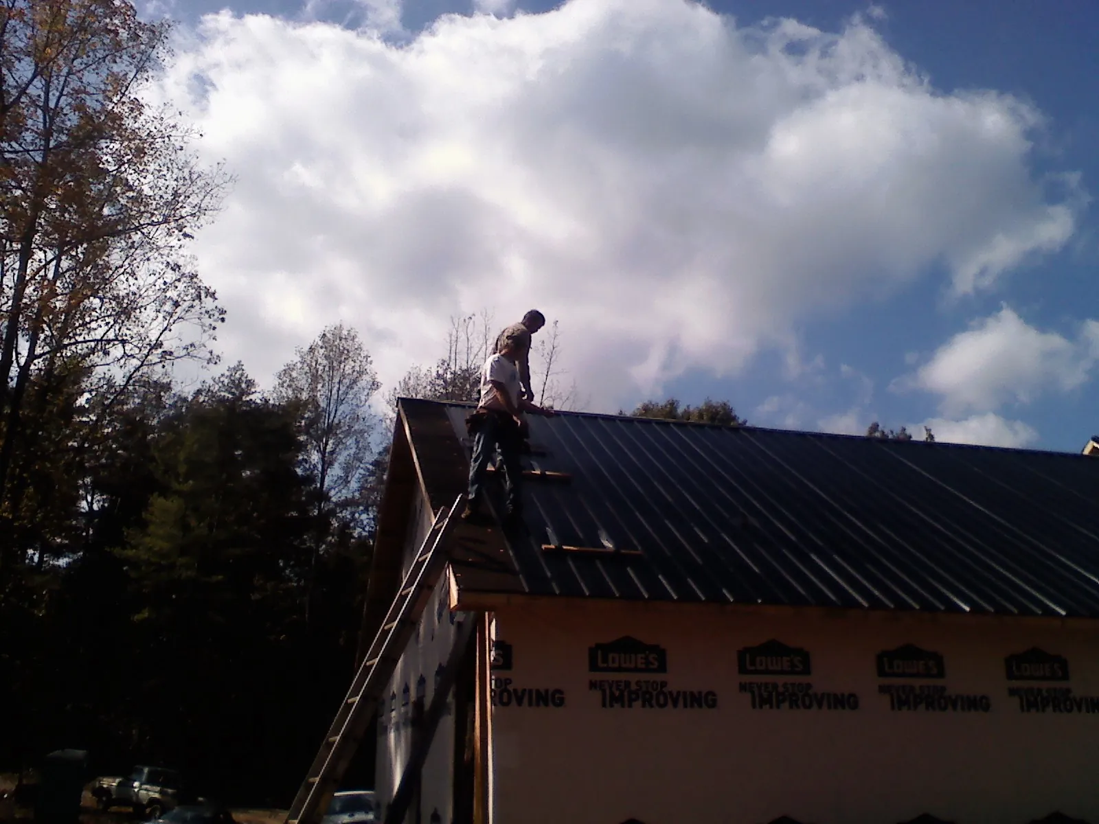 Roofer fastening dark metal panels high against a cloudy sky, from a Roof Inspection job in Social Circle