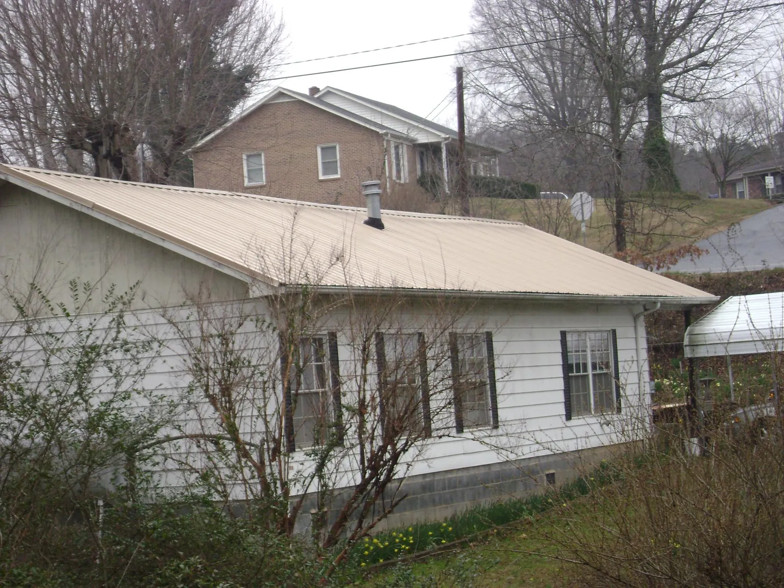 Tan metal roof on a white sided house set into a hillside — Commercial Roofing by Roofing Brothers in Social Circle